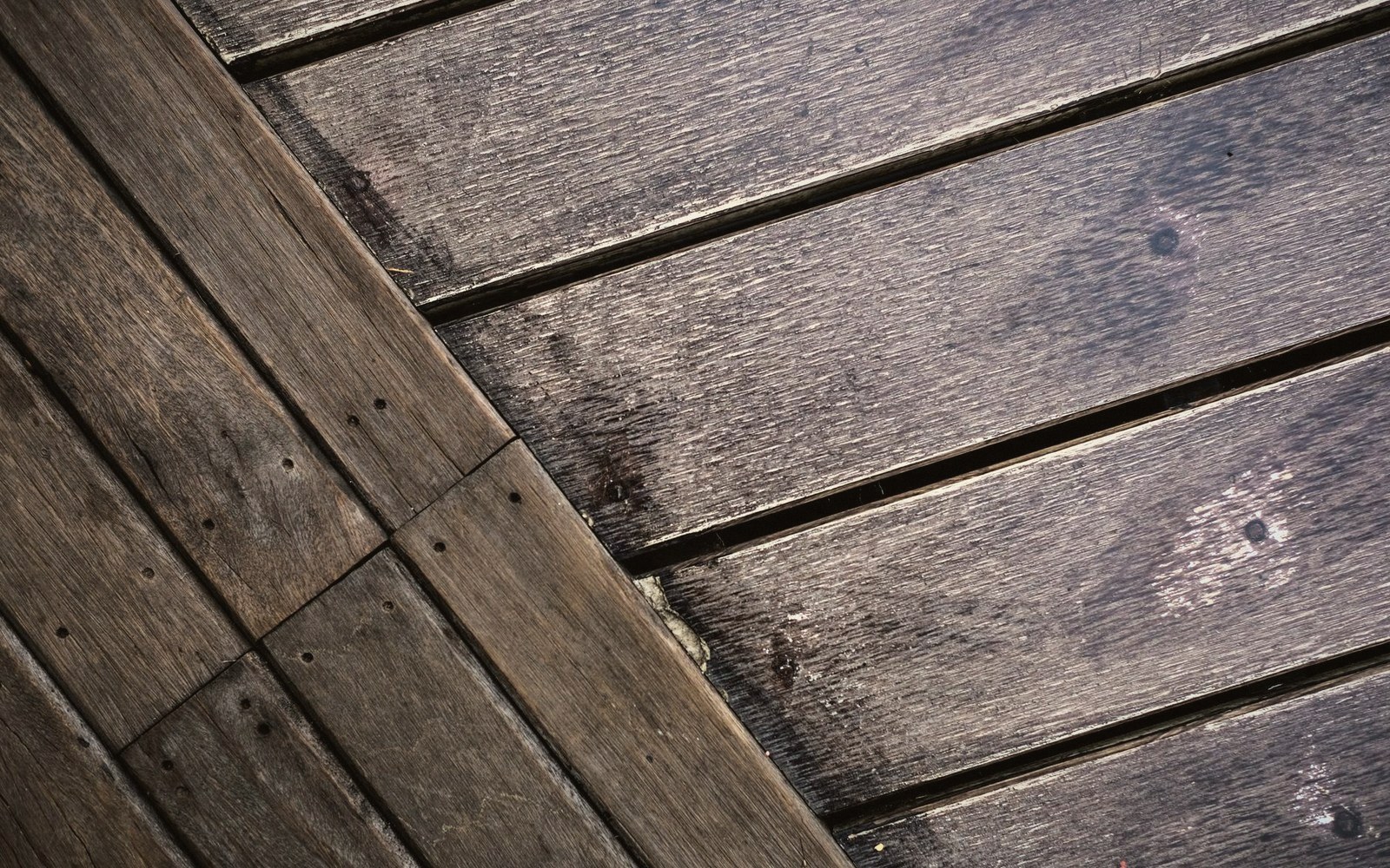 Weathered wooden deck boards meeting at a diagonal seam with visible nail heads